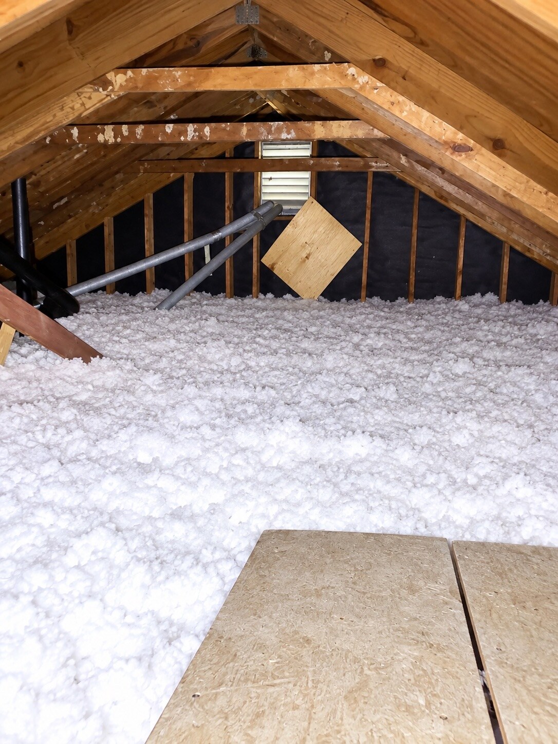 White blown-in fiberglass insulation covering an attic floor beneath exposed wooden roof framing