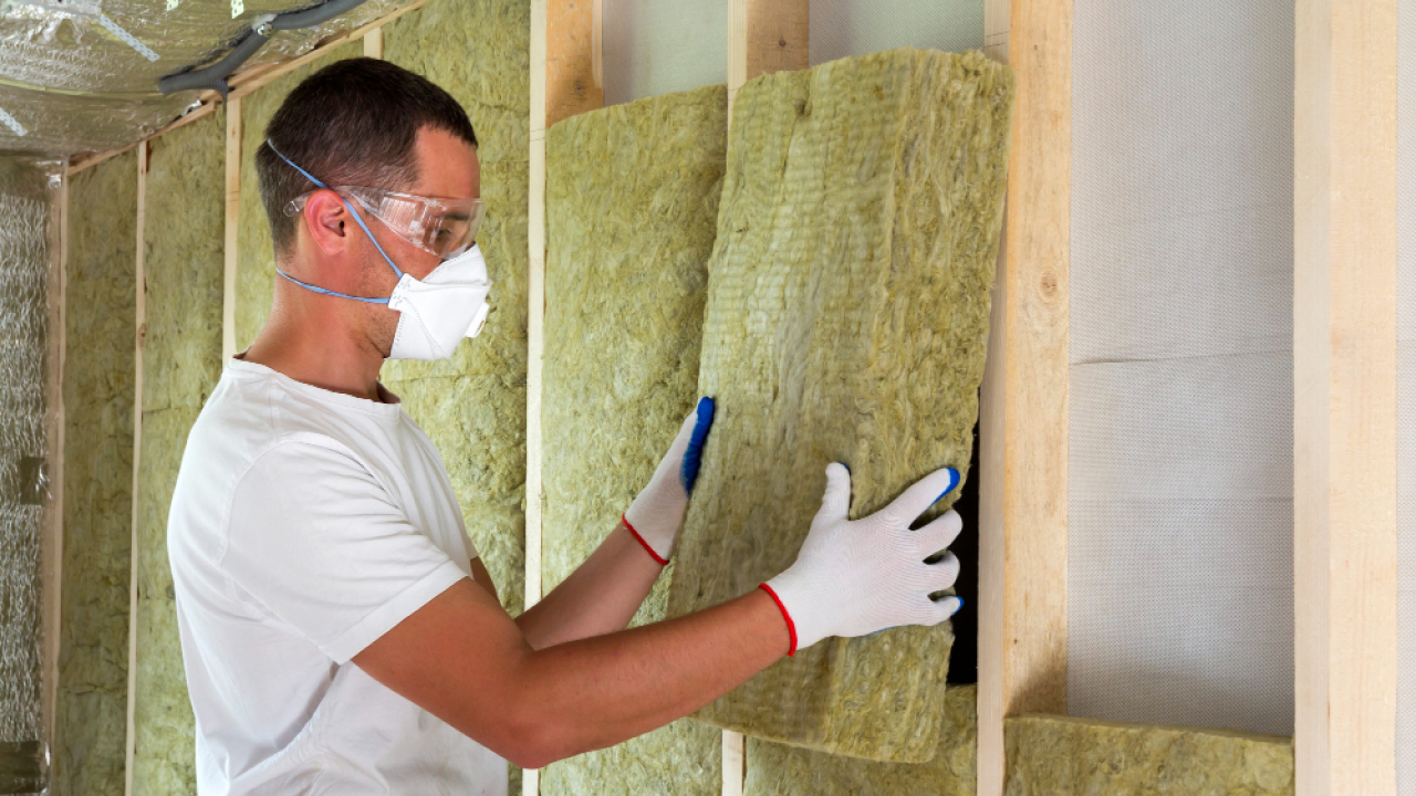 Worker in protective goggles and respirator insulating rock wool insulation